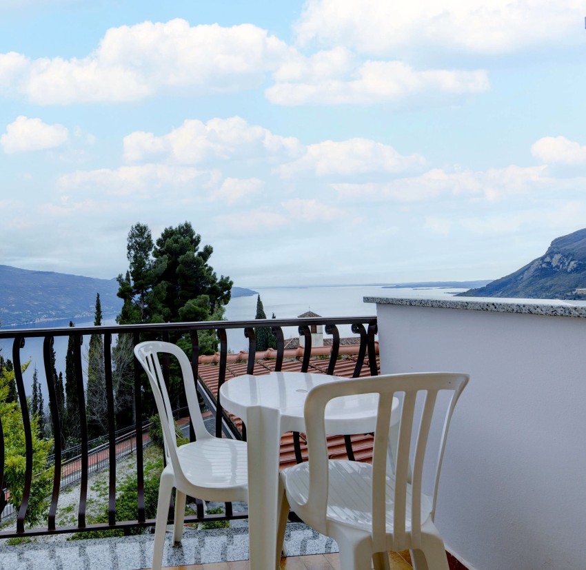 Balcony with plastic chairs overlooking Lake Garda and mountains.