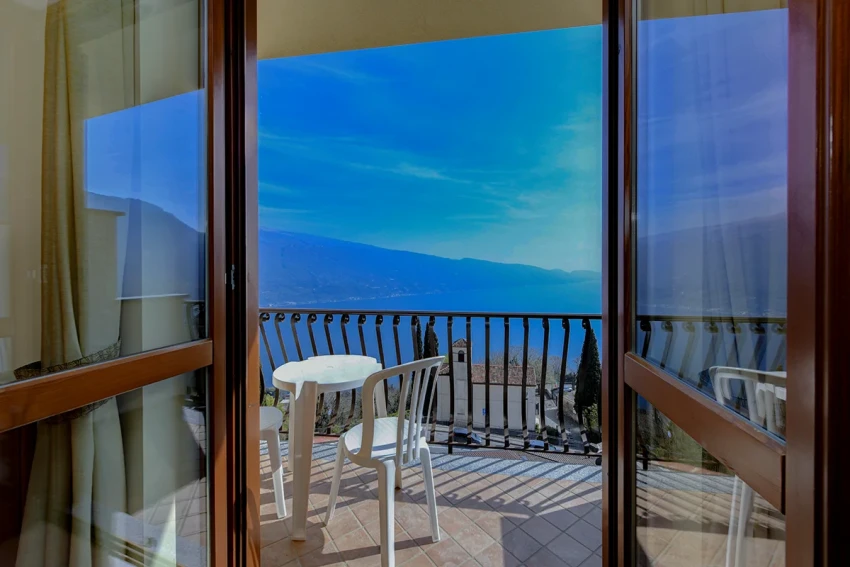 Balcony with table and chairs overlooking Lake Garda and mountains.