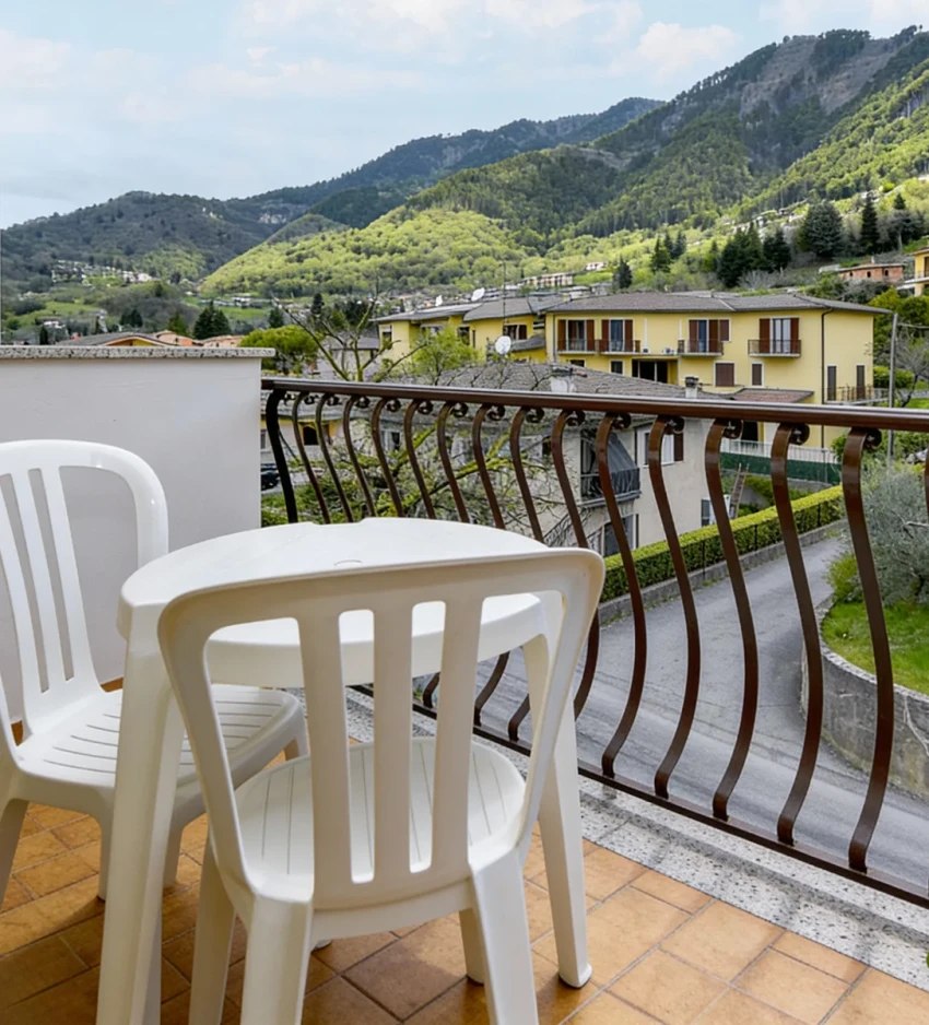 Balcony with white chairs and table overlooking green hills by Lago di Garda