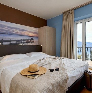 Bright double bedroom with balcony and Lake Garda view, hat and sunglasses on bed