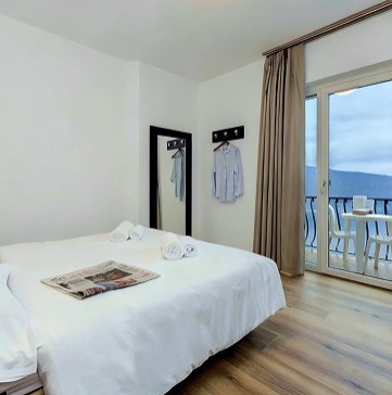 Bright bedroom with balcony overlooking Lago di Garda, bed and outdoor table.