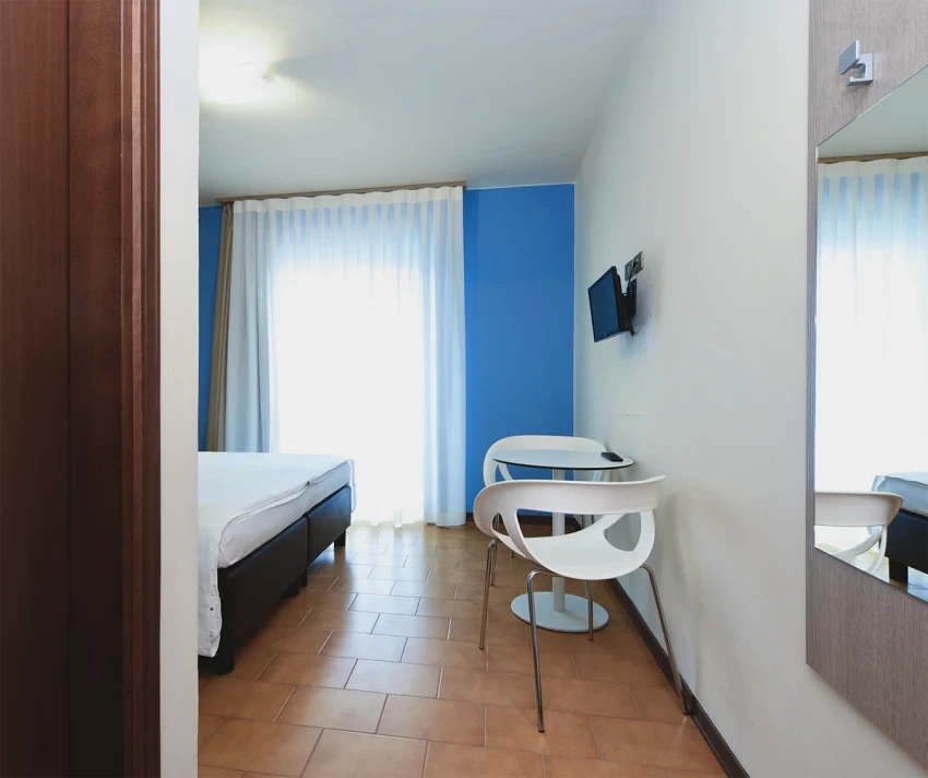 Bright hotel room with bed, chairs and TV near Lake Garda
