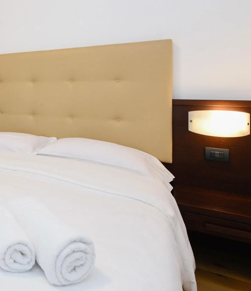 Camera d'hotel con letto matrimoniale, testiera beige e asciugamani vicino al Lago di Garda.