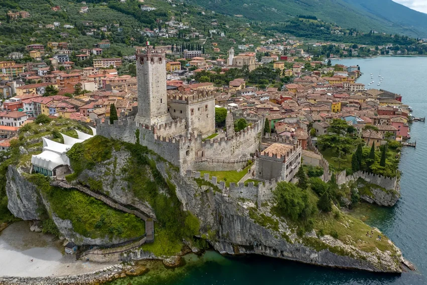 Castello medievale su scogliera con borgo e acqua turchese sul Lago di Garda