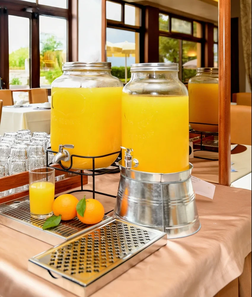 Due dispenser di succo d'arancia con bicchiere e arance al buffet, Lago di Garda