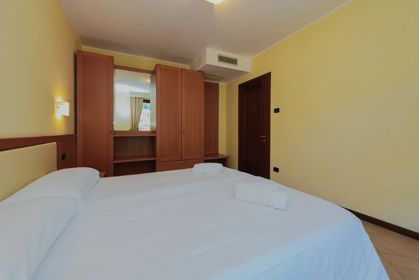Helles Doppelzimmer mit weißer Bettwäsche und Holzschrank, nahe dem Gardasee.