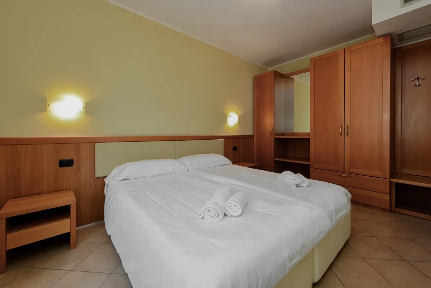 Doppelzimmer mit weißer Bettwäsche und Holzschränken am Lago di Garda