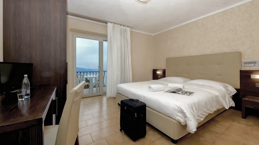 Hotel room with double bed, suitcase, and balcony overlooking Lake Garda