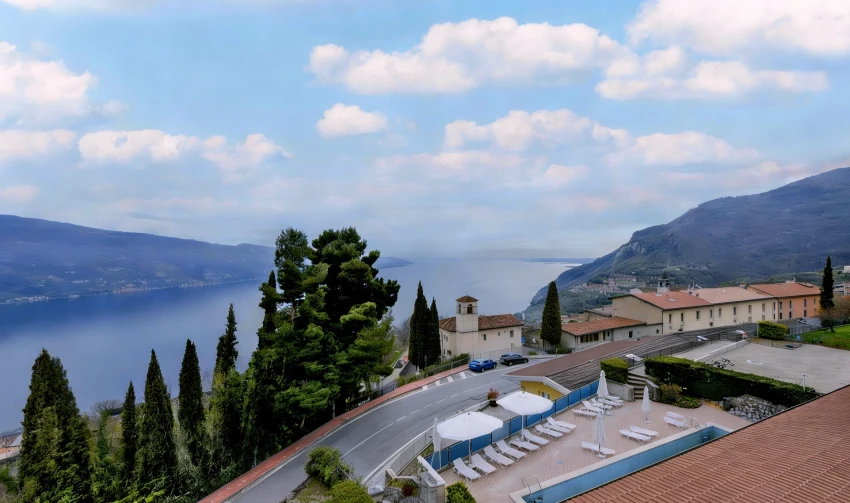 Panorama sul Lago di Garda con villaggio, cipressi e terrazza con piscina.