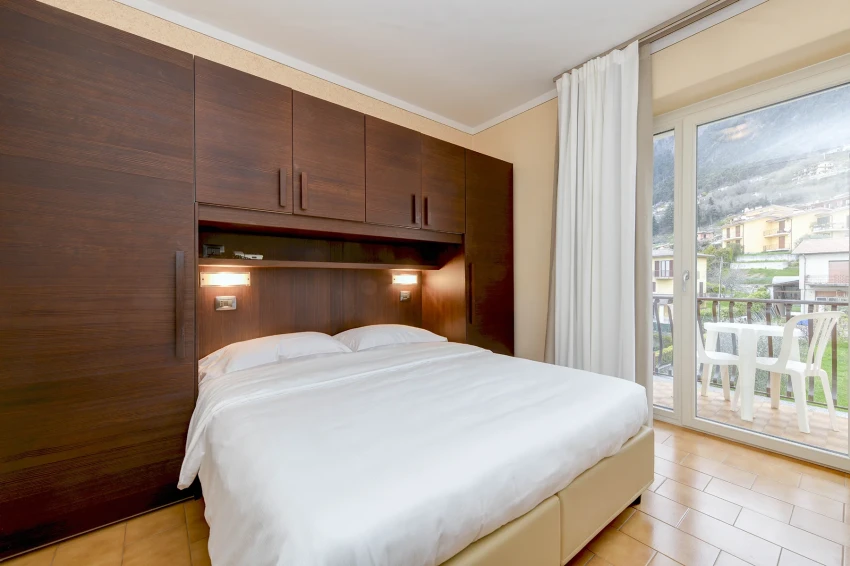 Helles Schlafzimmer mit Doppelbett, Holzschrank und Balkon, Blick auf den Gardasee