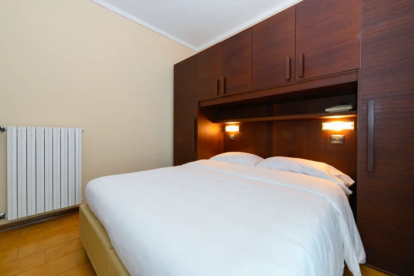 Schlafzimmer mit Doppelbett, Holzeinbauschrank und Leselampen nahe dem Lago di Garda